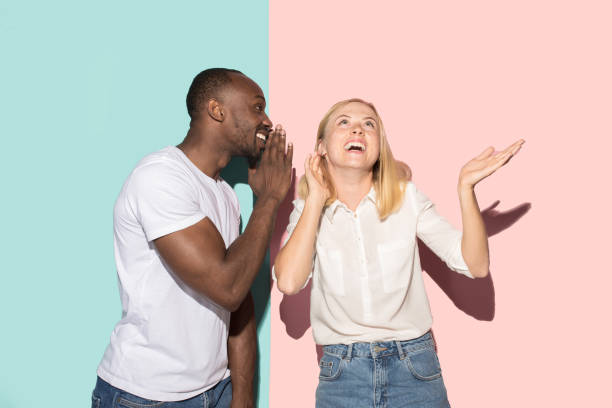 istock The young couple whispering a secret behind her hand over studio background 1009948486