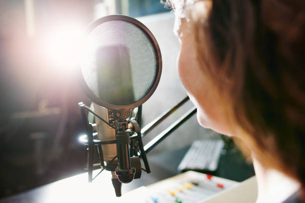 The magic happens behind the mic Shot of a woman speaking into a microphone in a recording studio commentator photos stock pictures, royalty-free photos & images