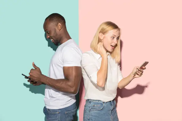 Photo of Mixed raced couple of students taking mobile phones. Caucasian girl and her African boyfriend posing at studio