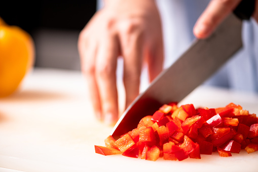 Woman chopping red pepper in kitchen. Young woman with large chief knife chopping red pepper on plastic board. Close up shot.