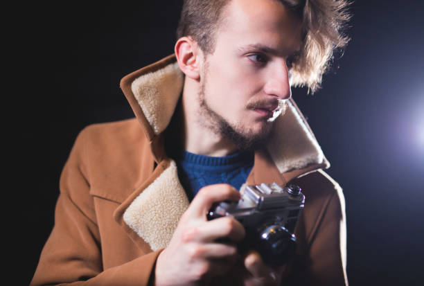 istock Young man with retro photo camera  in a coat on a black background. 1010010804