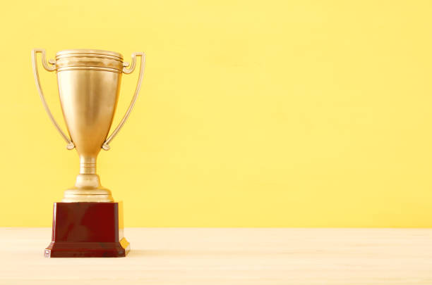 istock golden trophy over wooden table and yellow background. 1010015748