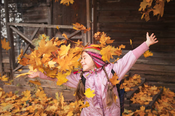 girl throws maple leaves. autumn fun. school holiday. child playing in leaf fall.