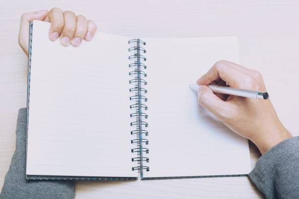 istock Mockup notepad and pen, female hands with pen writing on notebook Write notes wood table. View from above with copy space. 1010016178
