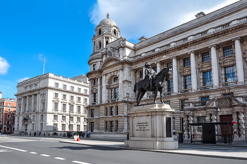 London, UK - May, 2023. People crossing street and sit on steps of monument at Piccadilly Circus Street in London during daytime in springtime with Piccadilly Circus Shopping center behind and huge advertisement board. British Flag and Coronation Flag  Landscape format.