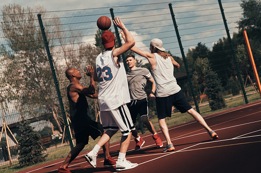 Group of young men in sports clothing playing basketball while spending time outdoors