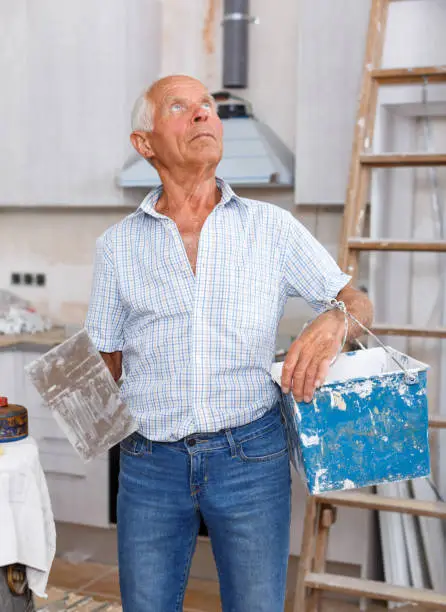 Senior man working on his house overhaul, determining scope of plastering works indoors