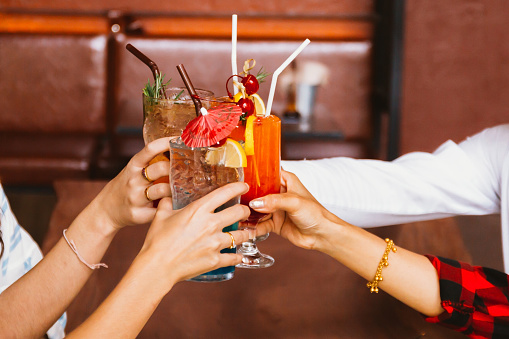 Close up of many friends hands holding a glass of alcoholic cocktail for social gathering and celebration in bar