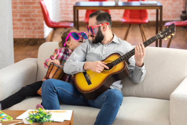 Little girl and her father with funny sunglasses playing instruments Little girl and her father with funny sunglasses sitting at home, playing a guitar and a drum. happy fathers day funny stock pictures, royalty-free photos & images