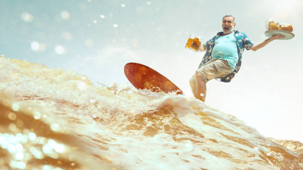 cin cin! concetto di vacanza. ritratto in studio di un bell'uomo anziano con barba grigia e cappello che tiene una bottiglia di birra - senior adult surfing aging process sport foto e immagini stock