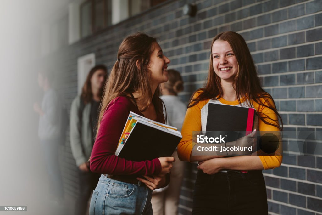 Female college students after lecture Portrait of smiling girls walking through high school corridor after their class. Two female college students after lecture. Teenager Stock Photo
