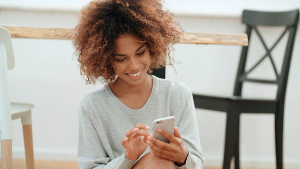 Beautiful young afro american woman using mobile phone at home. stock photo