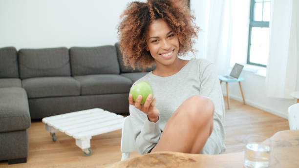 istock Young woman holding green apple while sitting at home. 1010059482