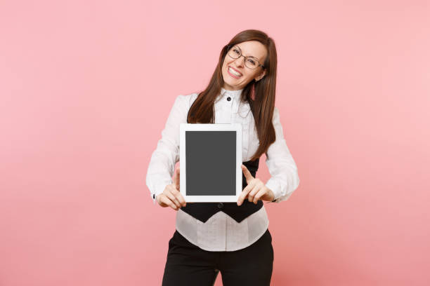 istock Young smiling business woman in glasses holding tablet pc computer with blank empty screen isolated on pink background. Lady boss. Achievement career wealth concept. Copy space for advertisement. 1010060128