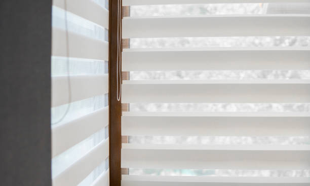 Details of white fabric roller blinds on the plastic window with wood texture in the living room. stock photo