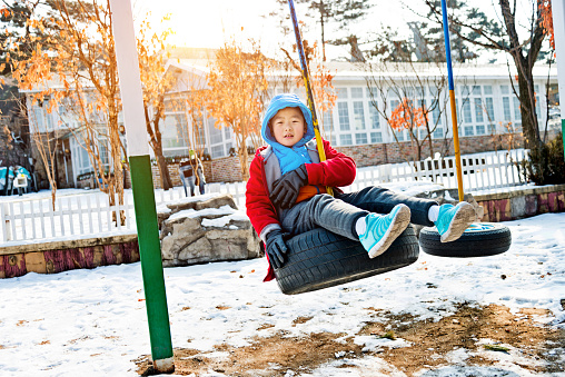 Boy playing on tire swing in winter day.