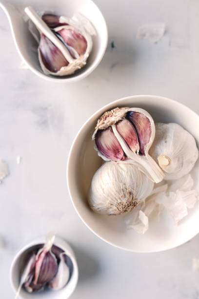 Garlic bulbs on a white table Garlic bulbs inside a bowl on a white table papery stock pictures, royalty-free photos & images