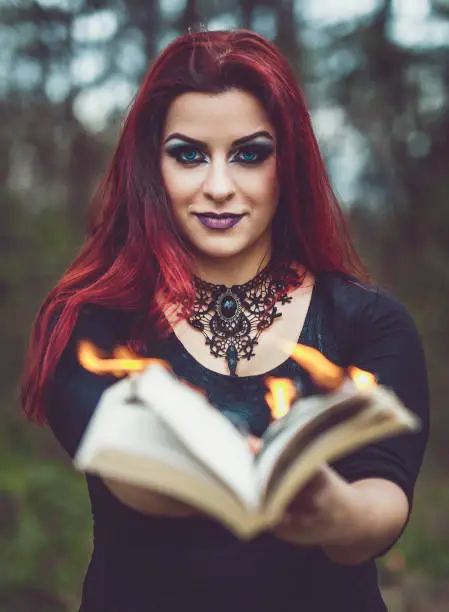 A redhead goth girl holding a book with pages aflame