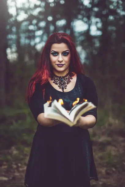 A redhead goth girl holding a book with pages aflame