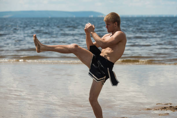 kickboxer tritt unter freiem himmel im sommer gegen das meer. - wushu action aggression power stock-fotos und bilder