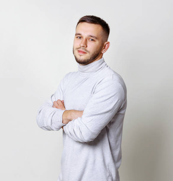 istock Friendly young man smiling in to the camera. Half side portrait handsome in white turtleneck and cross hands on breast. Copy space grey background 1010128828