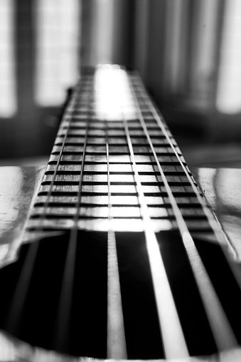Closeup of strings of a guitar illuminated by light entering from a window to the background