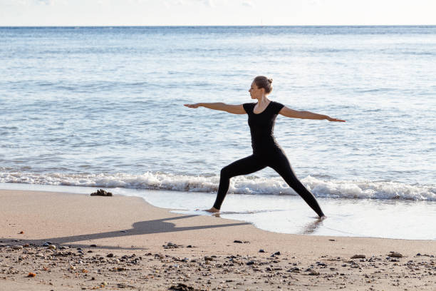 istock Young woman in black doing yoga on sand beach 1010142582