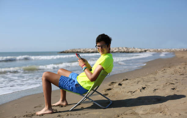 garçon lit un livre numérique en bord de mer - reading beach e reader men photos et images de collection