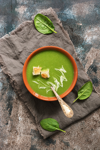 Traditional green cream soup with spinach is served with croutons. Rustic background, top view, flat lay