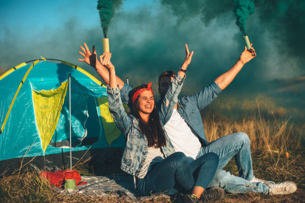 istock Young happy couple holding smoke bombs on camping 1010155028