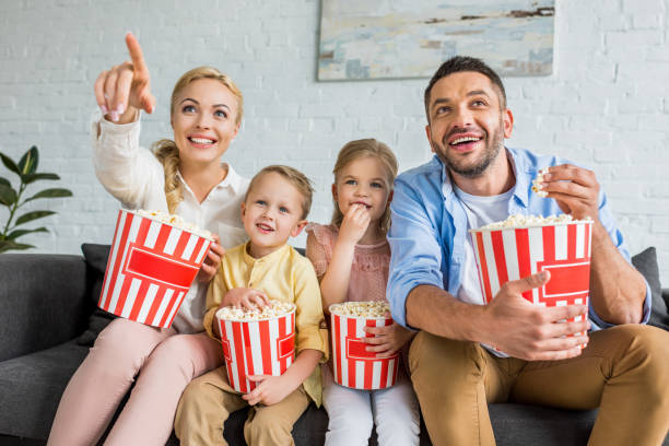 cheerful family eating popcorn and watching tv together at home - boyhood imagens e fotografias de stock