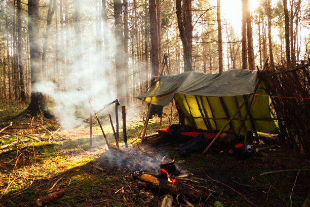 Smoke rising from a campfire in primitive tarp survival shelter stock photo