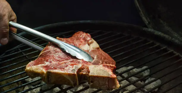 Someone Places a T-Bone Beef Steak on an Outdoor Barbecue Grill