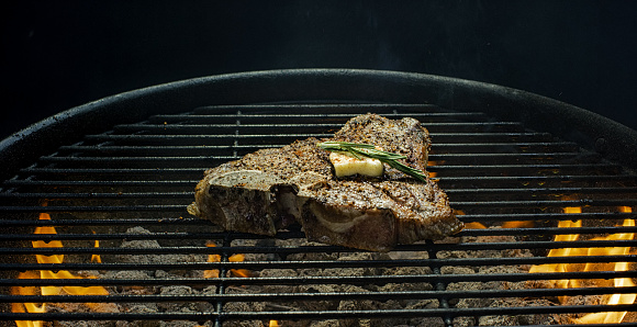 A Seasoned T-Bone Beef Steak with Butter and Rosemary Cooks Over Flaming Coals on a Barbecue Grill