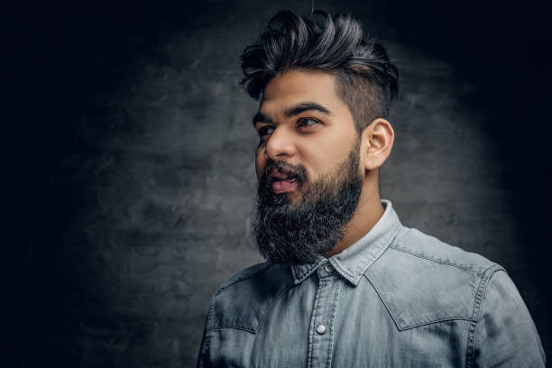 Studio portrait of stylish bearded Indian man in a blue shirt over grey background.