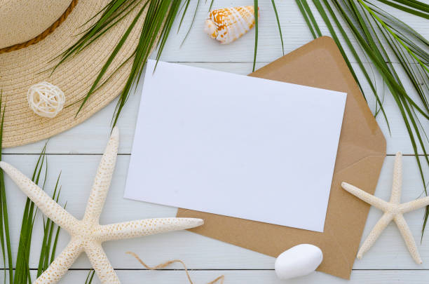 istock Mock up card template on white wooden background. Tropical palm leaf, summer hat, seastars and craft envelope. Invitation or greeting card concept 1010241204