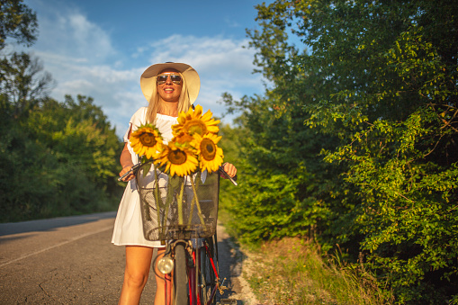 Young woman cycling on the road with a bunch of sunflowers