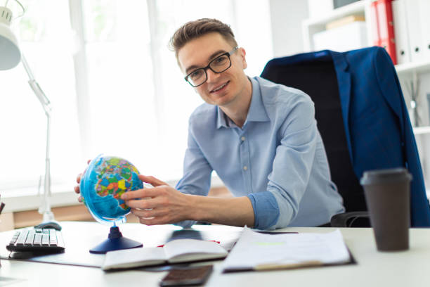 istock A young man sits in the office at a computer desk and holds a globe in his hands. 1010327104