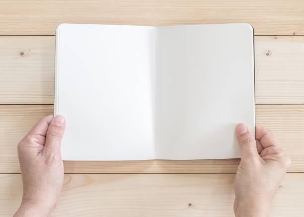istock Blank open pocket book mock up, catalog magazines, or note template with paper texture copyspace in person's hands on white pine wood table 1010329446