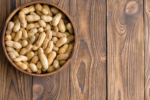 Bowl of whole natural raw peanuts in their shells on a wooden background with woodgrain pattern and copy space viewed from above