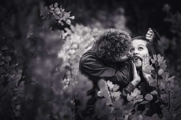 cheerful couple is naughty and shows emotions between autumn trees. curly-haired mustachioed man laughs and holds hair, and girl makes mustache out of her hair