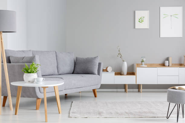 istock Table next to grey sofa in scandi living room interior with posters above cupboard. Real photo 1010339020
