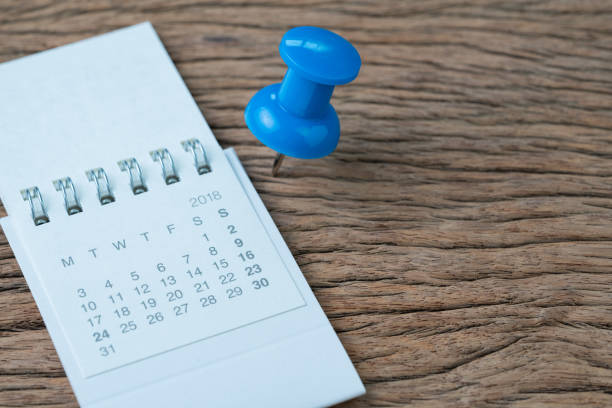 istock Date planning, appointment, deadline or holiday concept, big blue pushpin or thumbtack pin on wooden table next to white clean calendar 1010362586