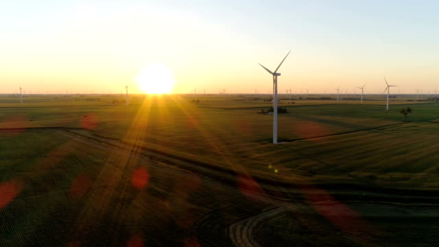 Aerial above countryside field and wind turbine into sunset with light beams