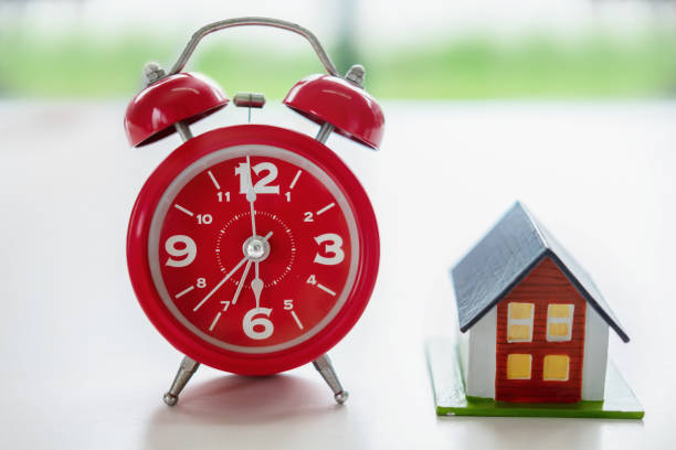 estate concept, red clock and model house on white table.