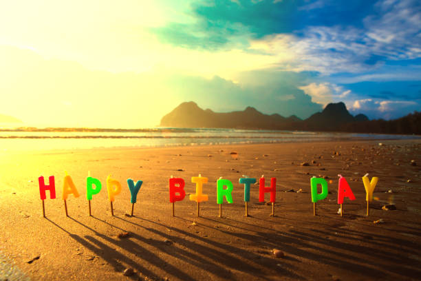 Happy birthday colorful candles on a beach sunrise. stock photo