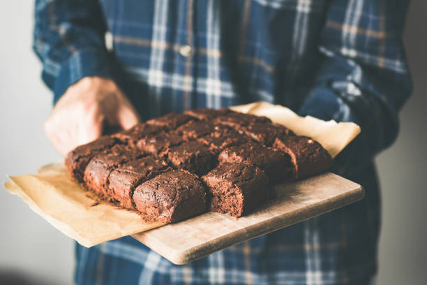 Vegan chocolate brownies on baking sheet. Young person holding plate with freshly baked vegan marijuana chocolate cakes