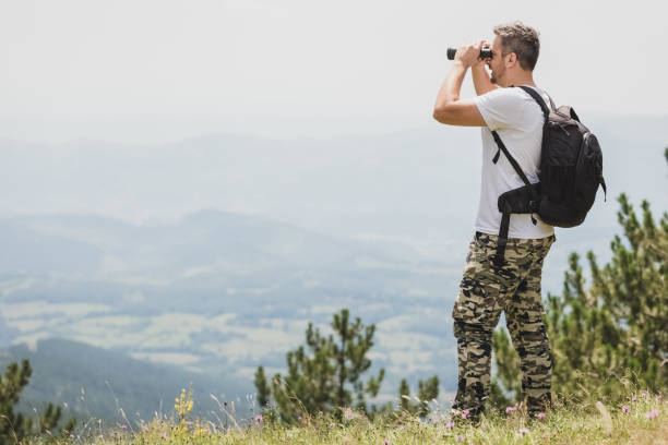 istock Traveler with backpack standing on the top of the mountain and using binoculars 1010485276