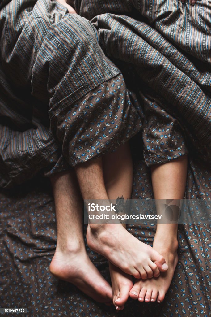 Legs of young couple lying in bed together in morning, romantic mood Sexual Issues Stock Photo