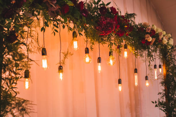 istock Wedding reception decoration with different electric edison lamps and fresh red and bordo flowers, rustic style 1010488416